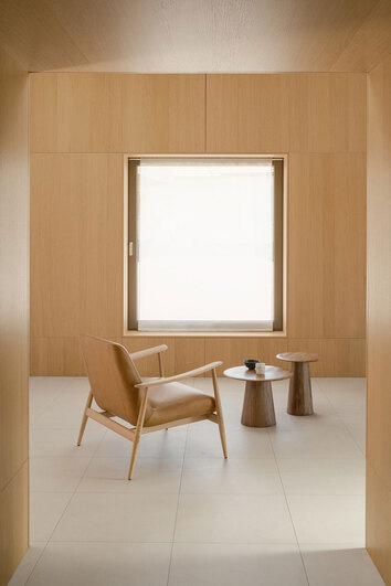 Aska Loungefåtölj i vitoljad ek klädd i lädret Dakar Nature i ett rum med väggar av träpaneler