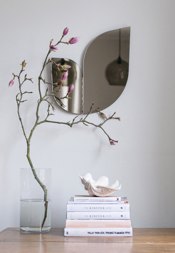 Perho Spegel på vägg ovanför en trave böcker och en vas med en kvist