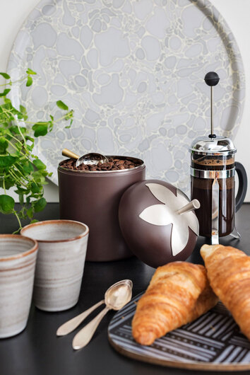 Blad Burk Stor med kaffebönor intill kaffekoppar, kaffepress och två croissanter