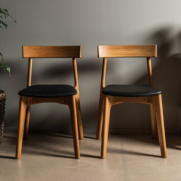 Två stycken K5 Stol i oljad ek mot en grå vägg