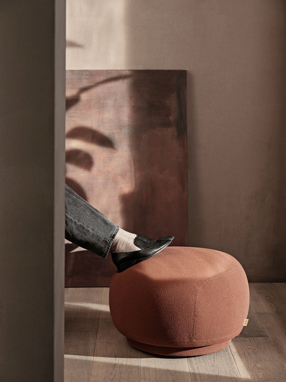 Rico Puff i tyget Grain Baked Clay med två fötter som vilar på puffen