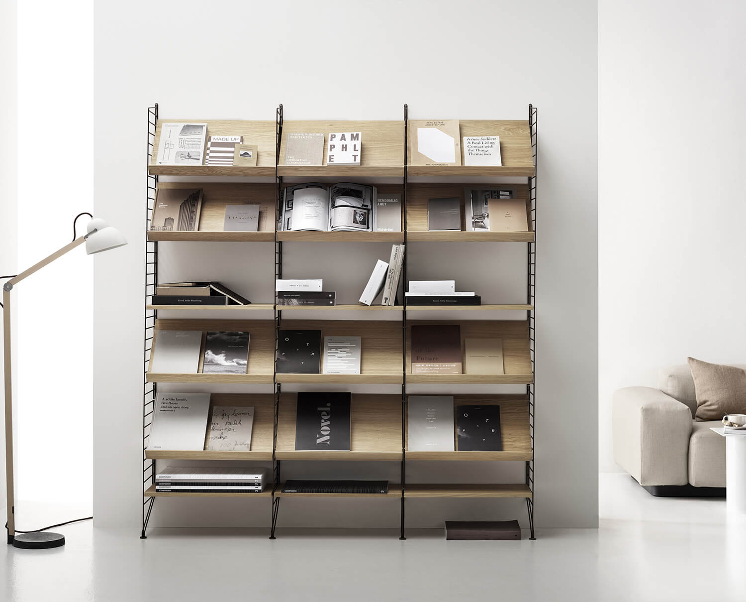 String bokhylla med tidsskriftshyllor i ask ståendes i ett vitt vardagsrum med tillhörande inredning.