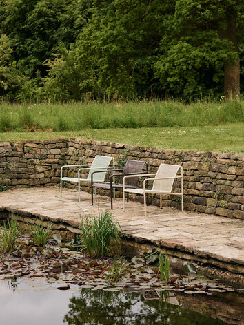 Dapple Loungestol i färgen Tea Green, Dark Chocolate och Cashmere som står på en rad bredvid en damm