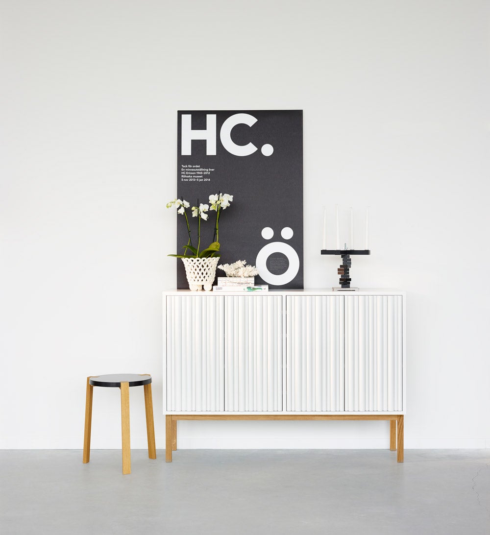 Collect 2013 Skåp Lågt Vit / Oljad Ek bredvid en pall. Det hänger en tavla med grafiskt motiv ovanför.