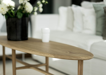 Crest Soffbord Ovalt i massiv ek i en miljöbild där bordet är stylat med en stor blombukett med vita blommor. soffbrodet matchas mot en vit soffa.