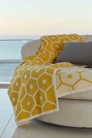 Honey Pläd Lemon på beige fåtölj framför fönster med havsutsikt